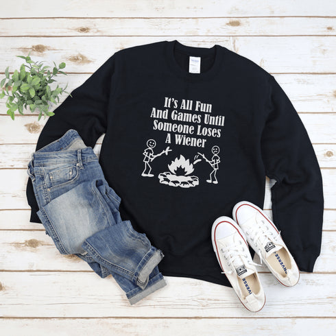 Our Camping sweatshirt features two stick people roasting wieners over a campfire with the hilarious saying, "It's All Fun & Games Until Someone Loses A Wiener."